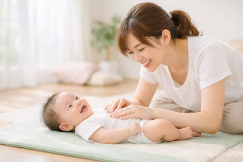 明るい室内でマットの上に寝た赤ちゃんとママが楽しそうに親子ふれあい運動。赤ちゃんは笑顔で仰向け、ママが優しく手を添えてベビーマッサージ。自然光とパステルカラーの穏やかな雰囲気で、安心して参加できる0歳親子向け体験イベント
