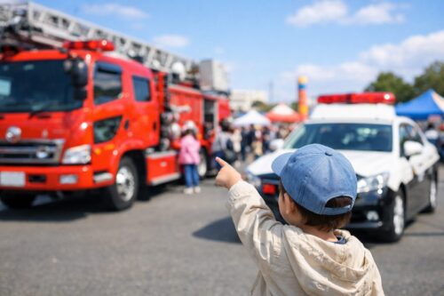 消防車やパトカーを指差して見上げる子どもの後ろ姿